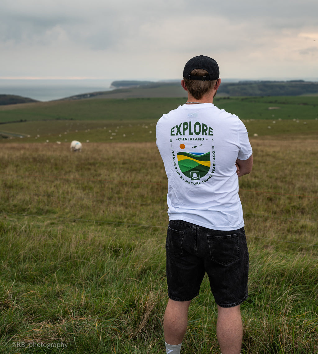 Person wearing a white t-shirt with 'EXPLORE' on the back, standing in a grassy field.
