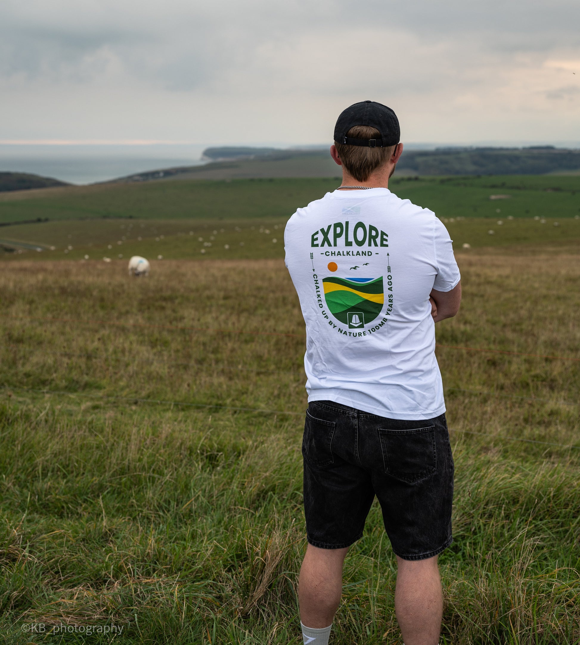 Person wearing a white t-shirt with 'EXPLORE' on the back, standing in a grassy field.