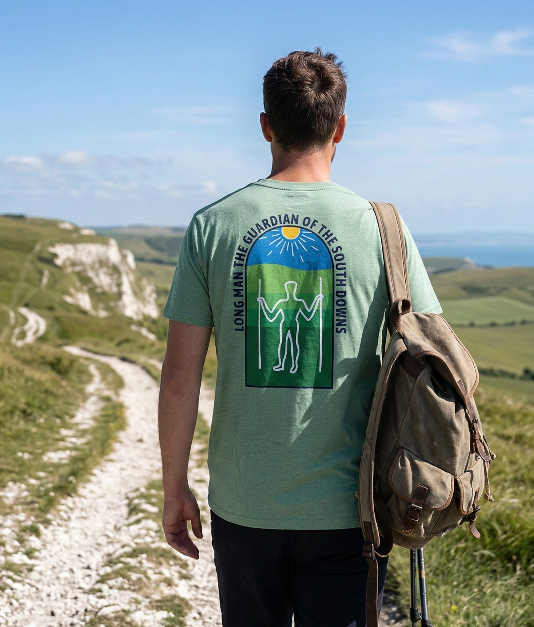 Man walking on a path with a scenic view, wearing a green t-shirt with a logo and text.