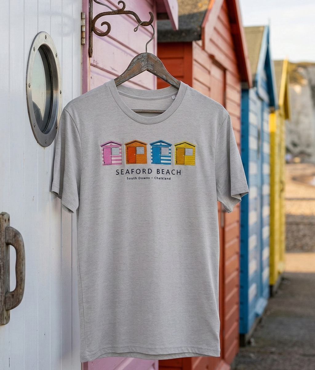 Gray t-shirt with colorful text design hanging on a wooden post with beach huts in the background