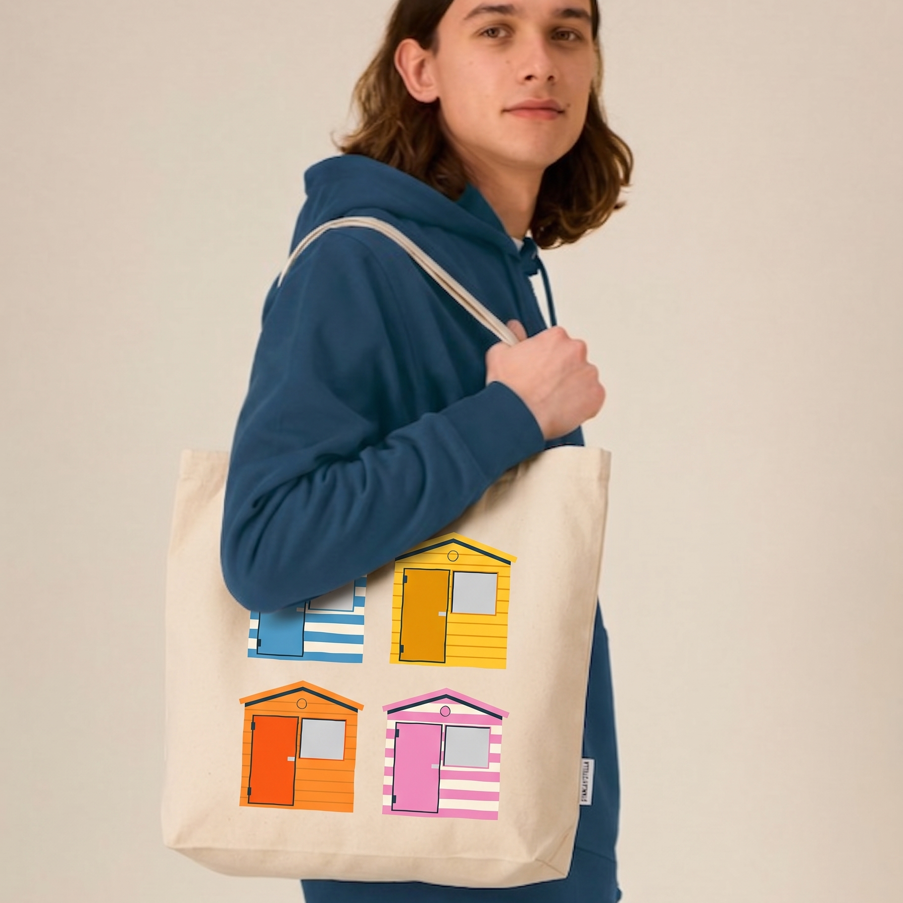 Person holding a tote bag with colorful beach hut design against a beige background