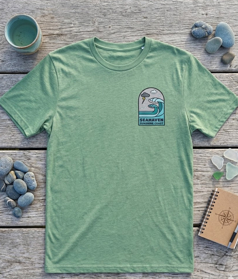Green t-shirt with a graphic design on a wooden surface with rocks and a notebook.