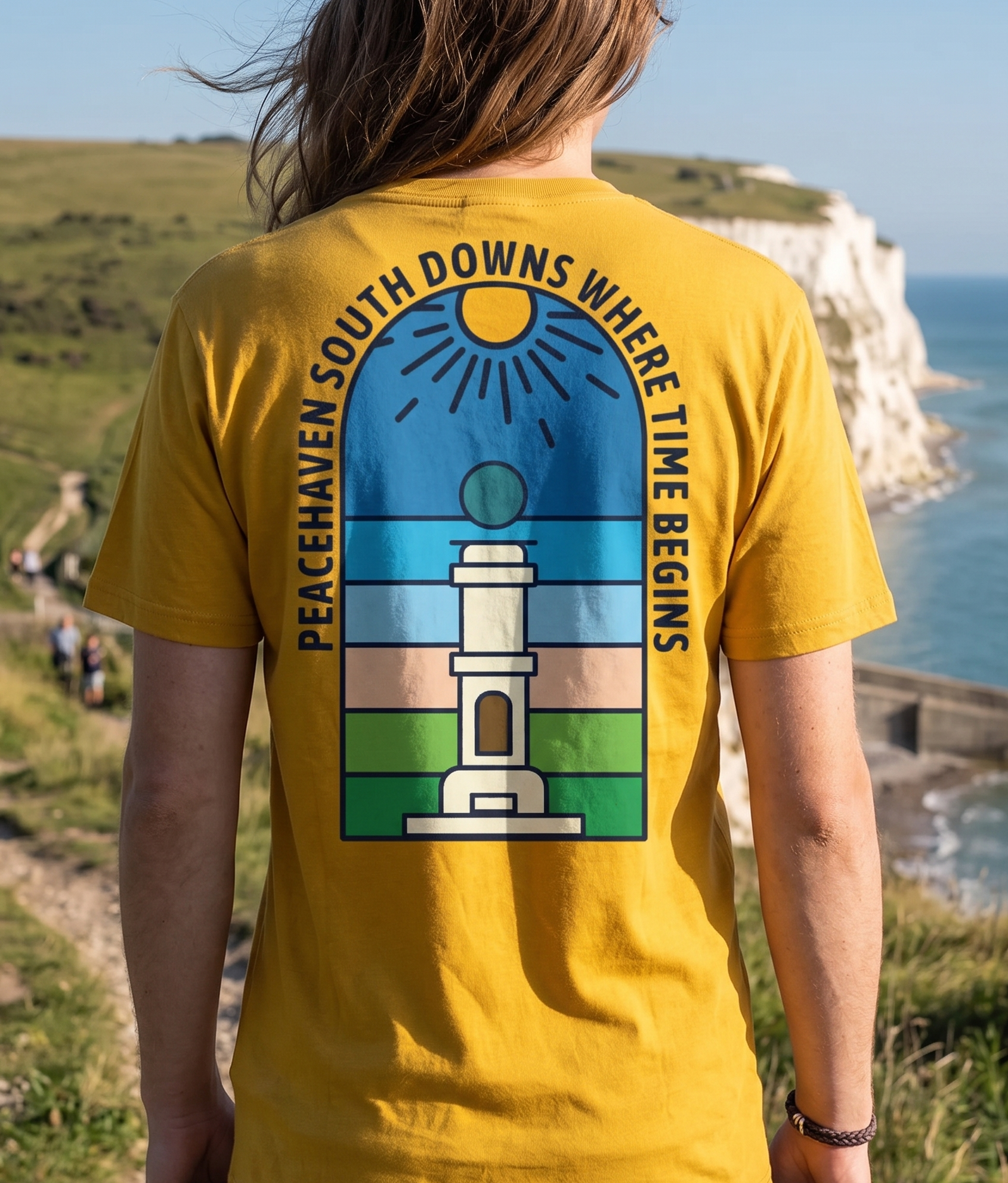 Person wearing a yellow t-shirt with a scenic design and text, standing on a cliff overlooking the sea.